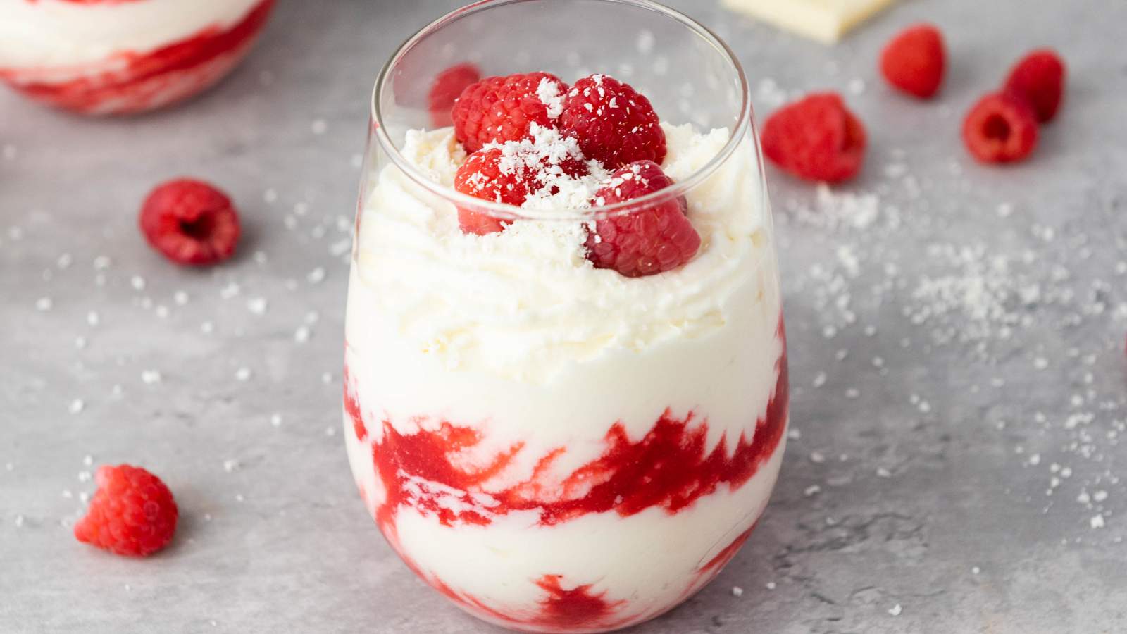A glass filled with white chocolate raspberry mousse, topped with fresh raspberries and a sprinkle of white shavings.