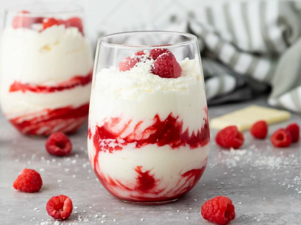A glass filled with white chocolate raspberry mousse, topped with fresh raspberries.