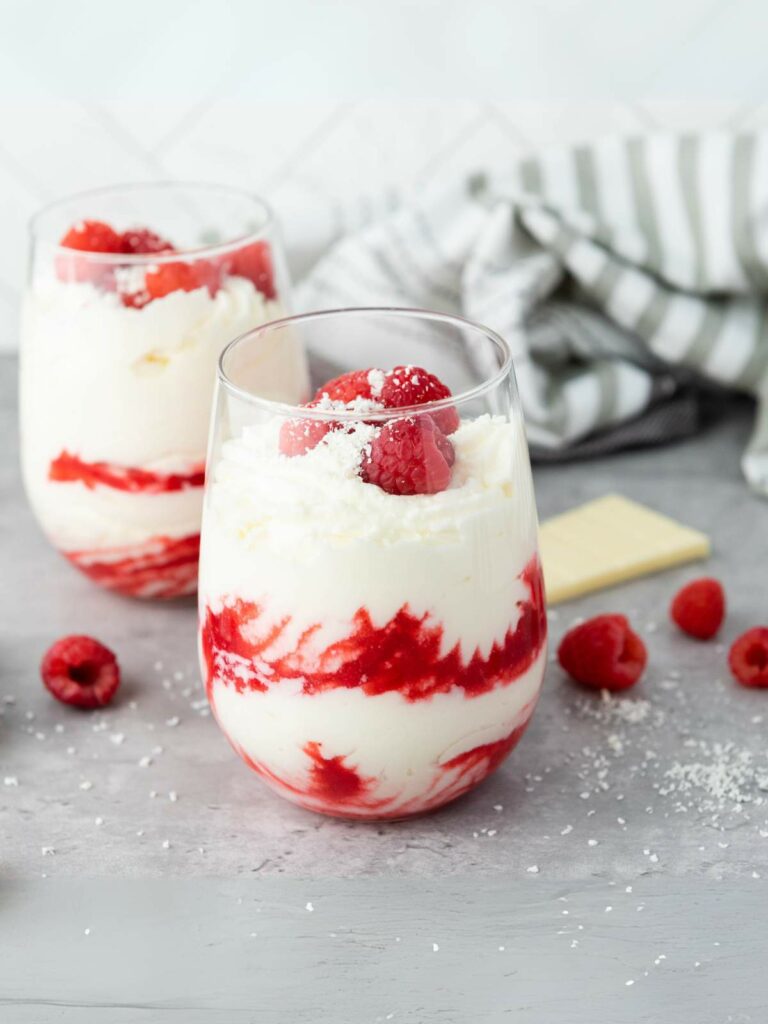 Two glasses filled with white chocolate raspberry mousse, topped with fresh raspberries.