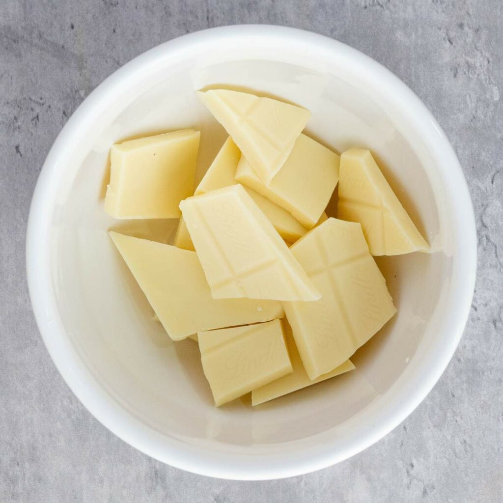 A white bowl containing several pieces of white chocolate, placed on a gray textured surface.