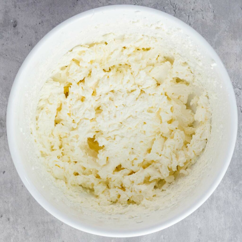 A white mixing bowl containing creamed butter and sugar on a gray countertop.