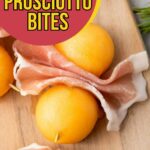 Two pieces of prosciutto are wrapped around yellow melon balls on a wooden board, garnished with rosemary.
