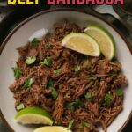 A bowl of shredded beef barbacoa garnished with chopped cilantro and lime wedges, viewed from above.