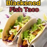 Two soft tacos filled with blackened fish, shredded purple cabbage, onions, cilantro, and creamy green sauce.