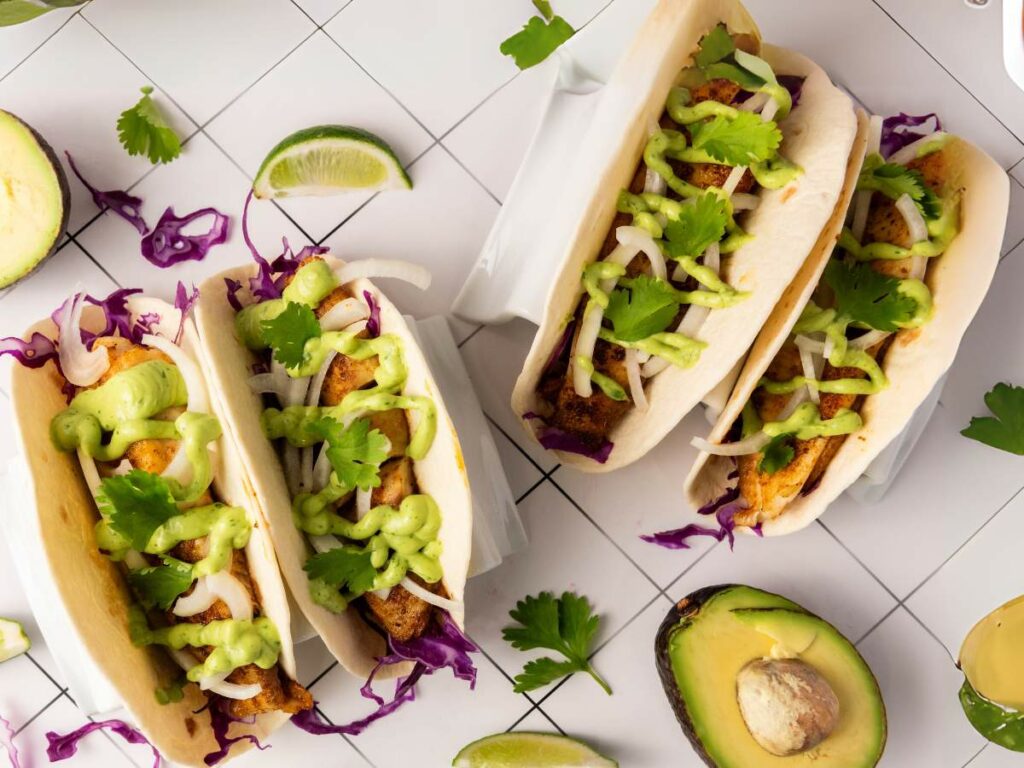 Three fish tacos filled with cabbage, onion, cilantro, and green sauce.
