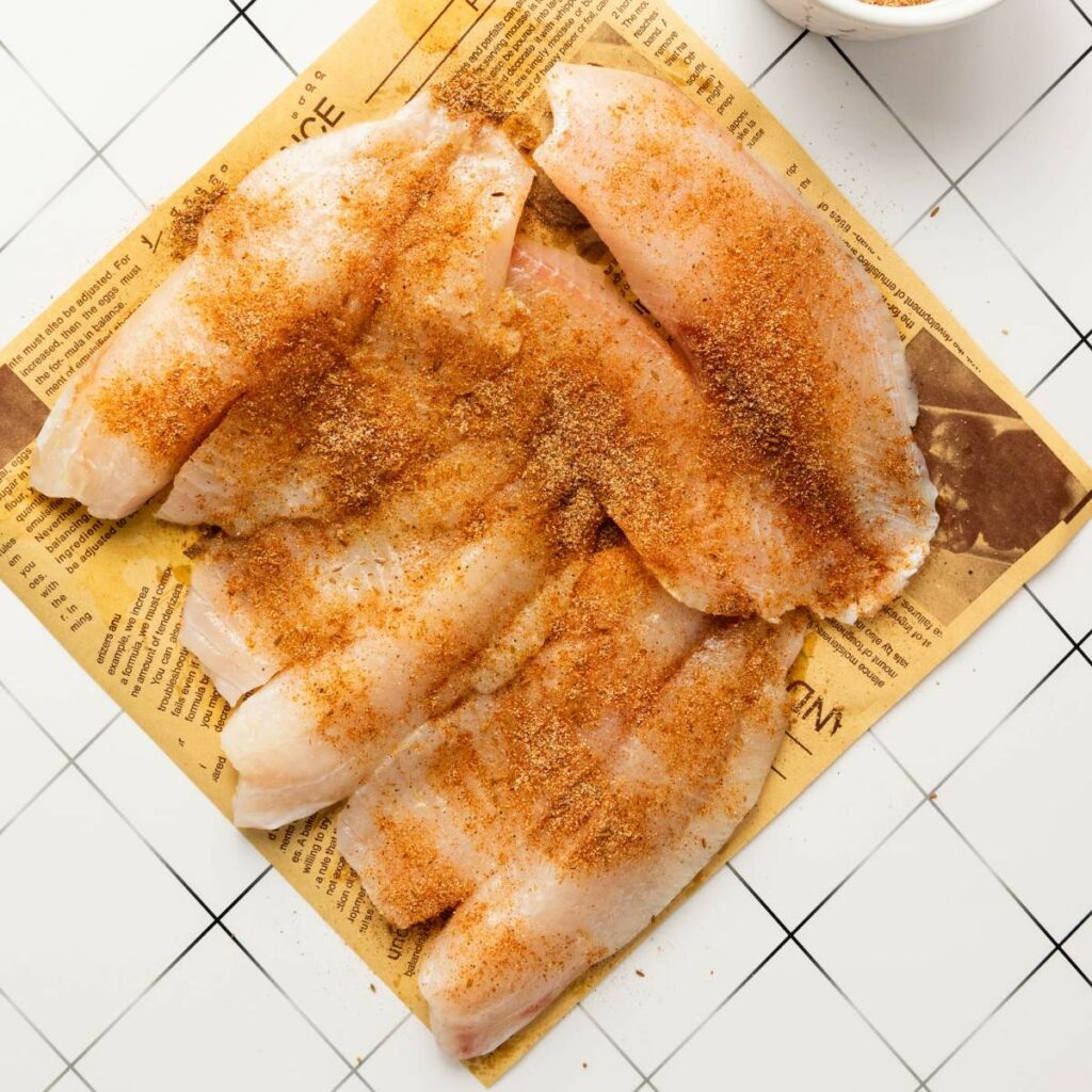 Raw fish fillets laid out on newspaper and sprinkled with seasoning.