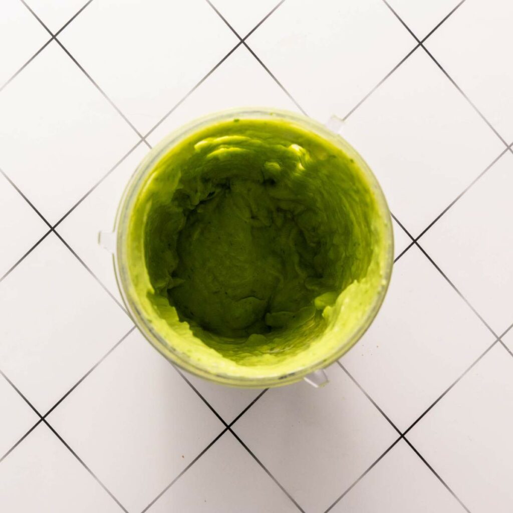 Top-down view of a blender cup filled with smooth, green avocado puree.