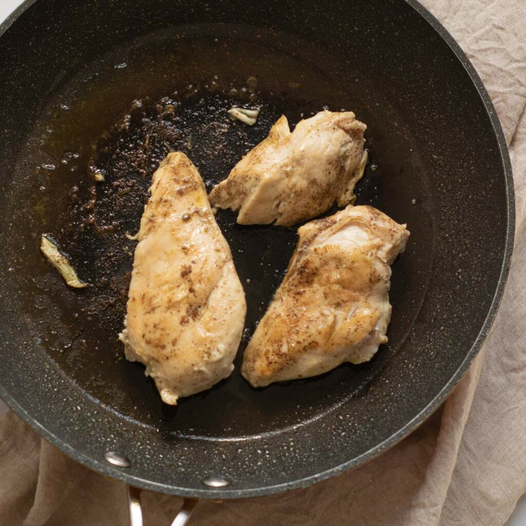 Three seasoned chicken breasts cooking in a black frying pan.