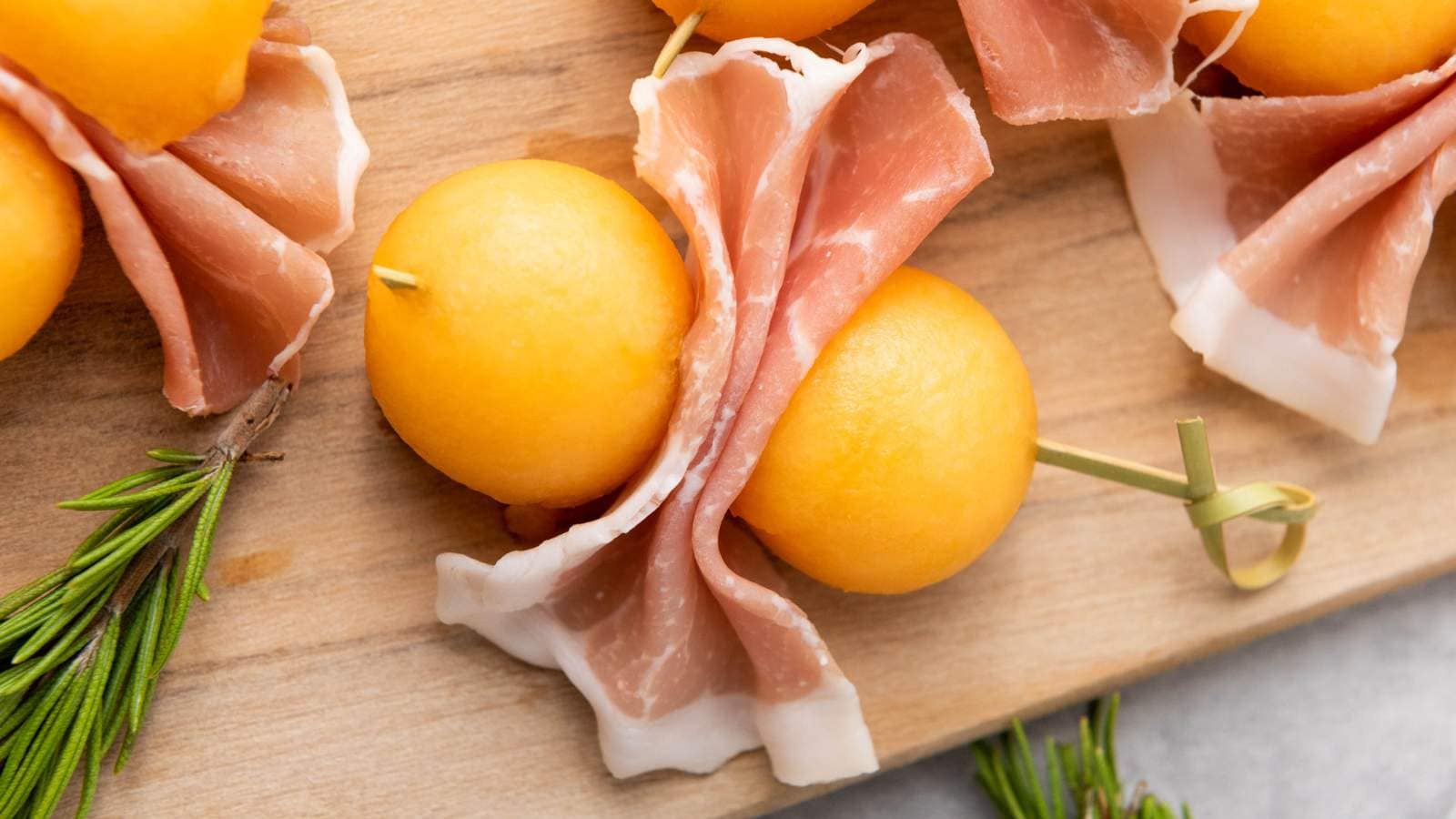 Slices of prosciutto wrapped around cantaloupe balls and skewered with toothpicks.