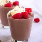 A glass of protein pudding topped with whipped cream, fresh raspberries,.