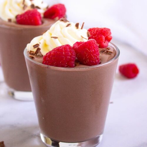 A glass of protein pudding topped with whipped cream, fresh raspberries,.