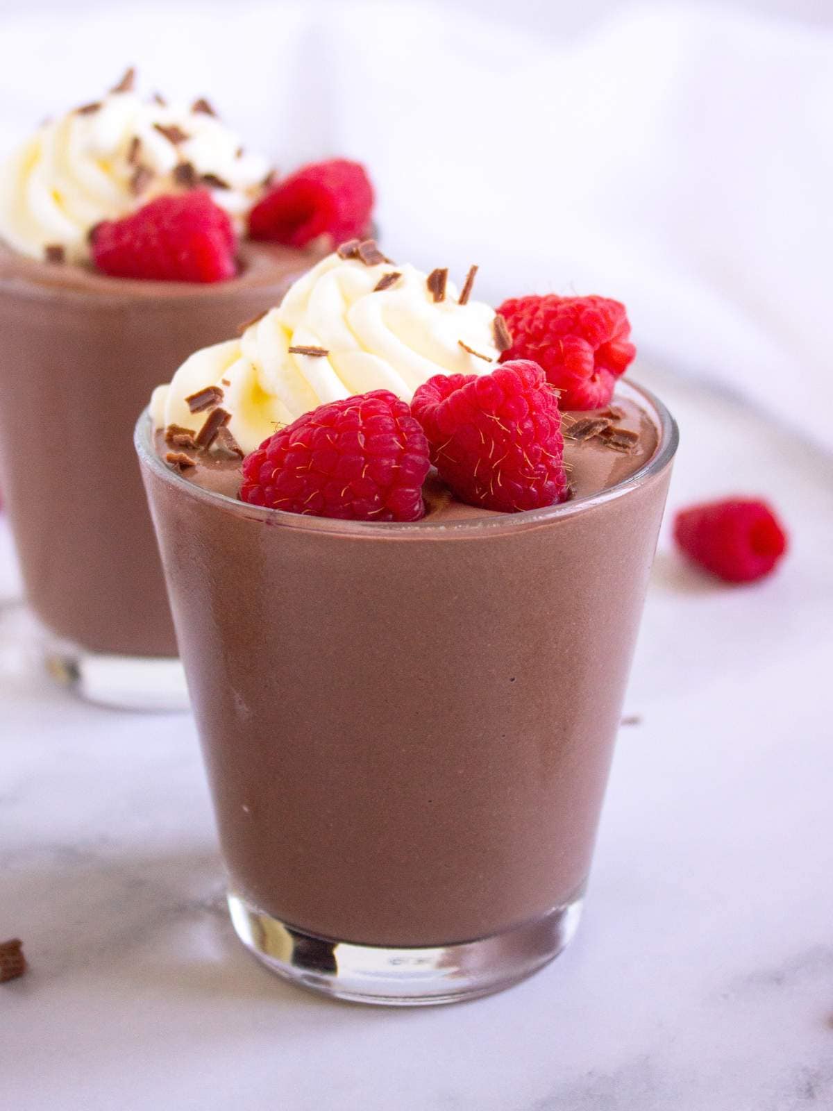A glass of protein pudding topped with whipped cream, fresh raspberries,.