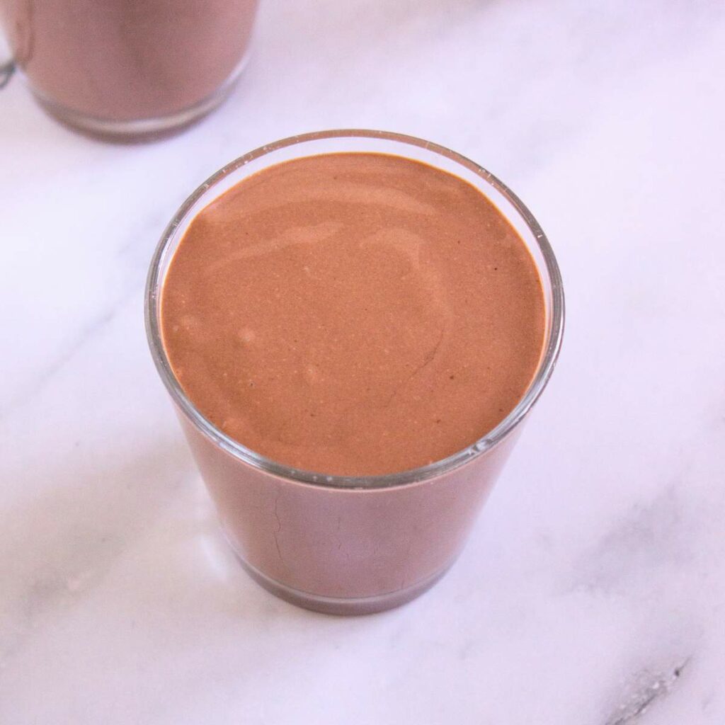 A glass filled with chocolate smoothie sits on a white marble surface.