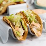 Two smash burger taco filled with grilled meat, shredded lettuce, and creamy sauce.