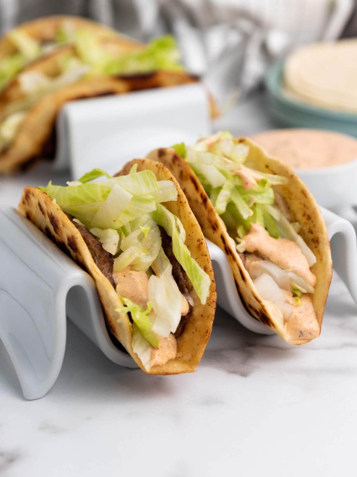 Two smash burger taco filled with grilled meat, shredded lettuce, and creamy sauce.