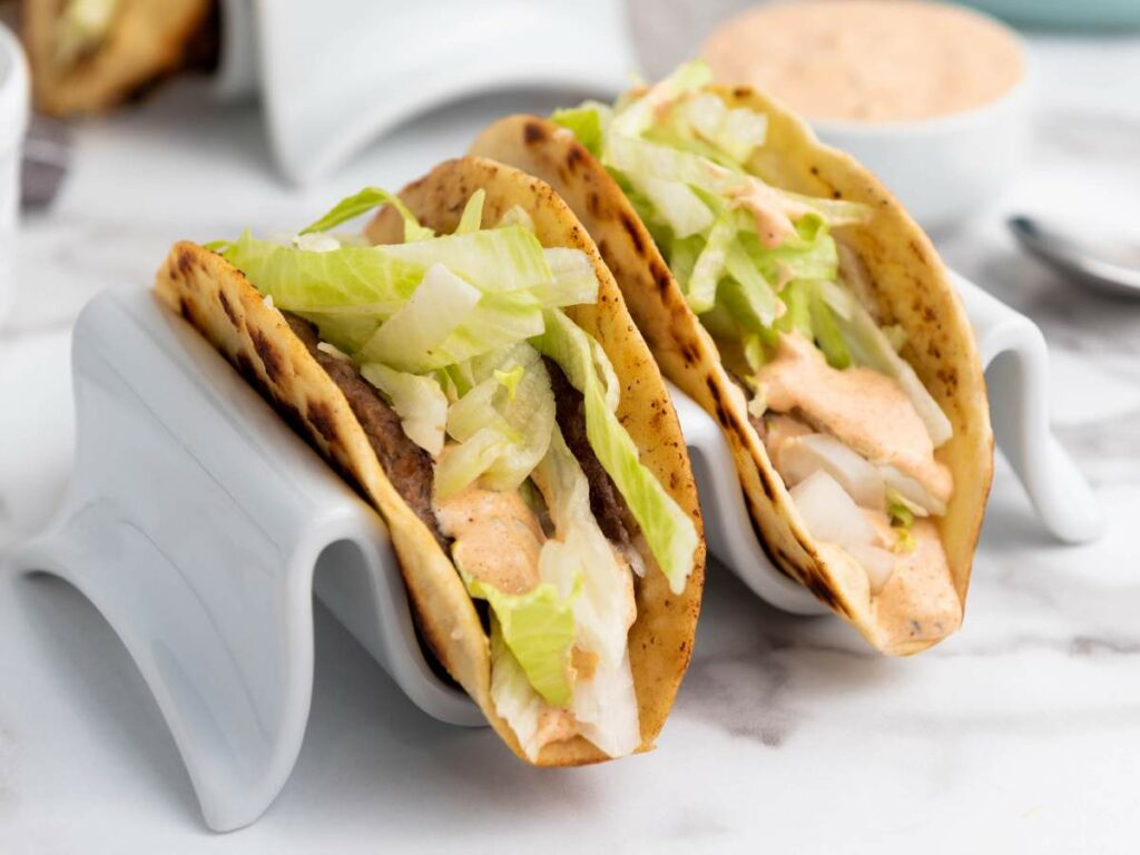 Two smash burger taco filled with lettuce, onions, and sauce.