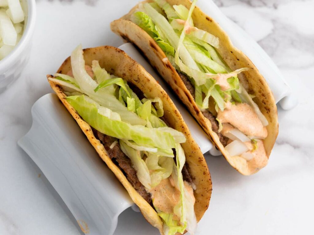 Two smash burger tacos in crispy shells topped with shredded lettuce and a creamy sauce.