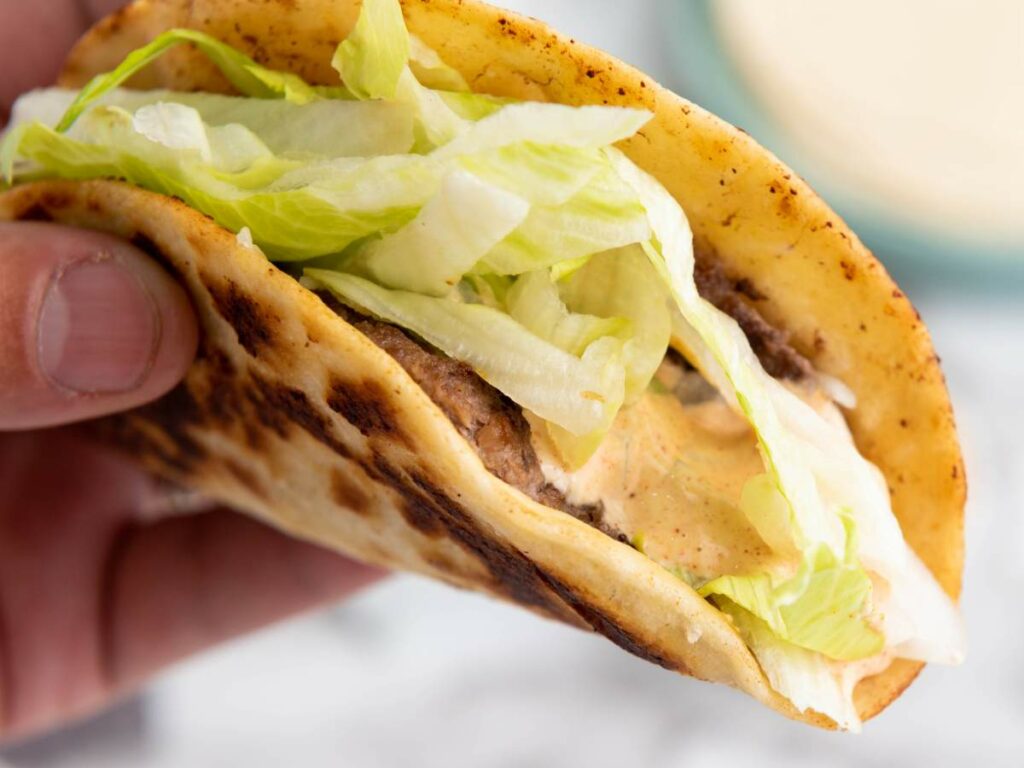 Smash burger taco with ground beef, shredded lettuce, sauce, and a toasted taco shell.