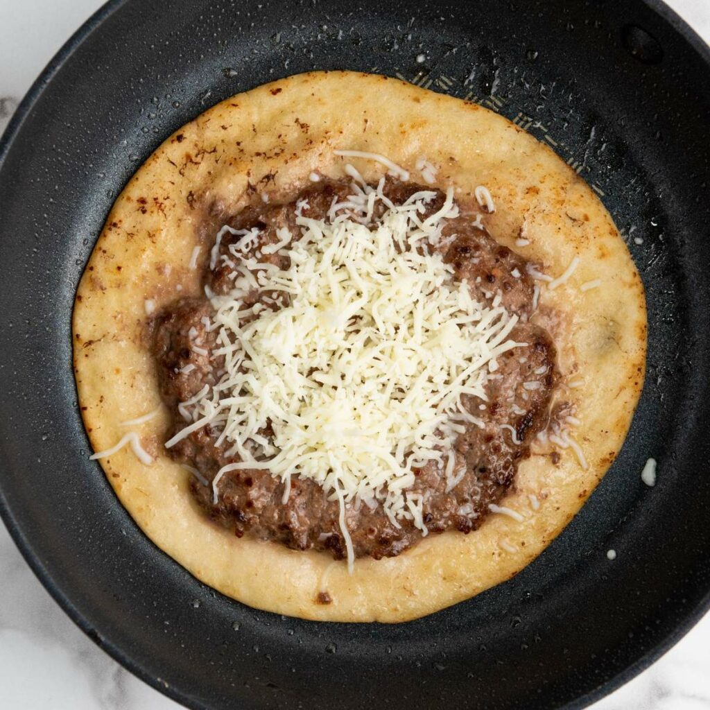 A skillet with a flatbread topped with refried beans and shredded cheese.