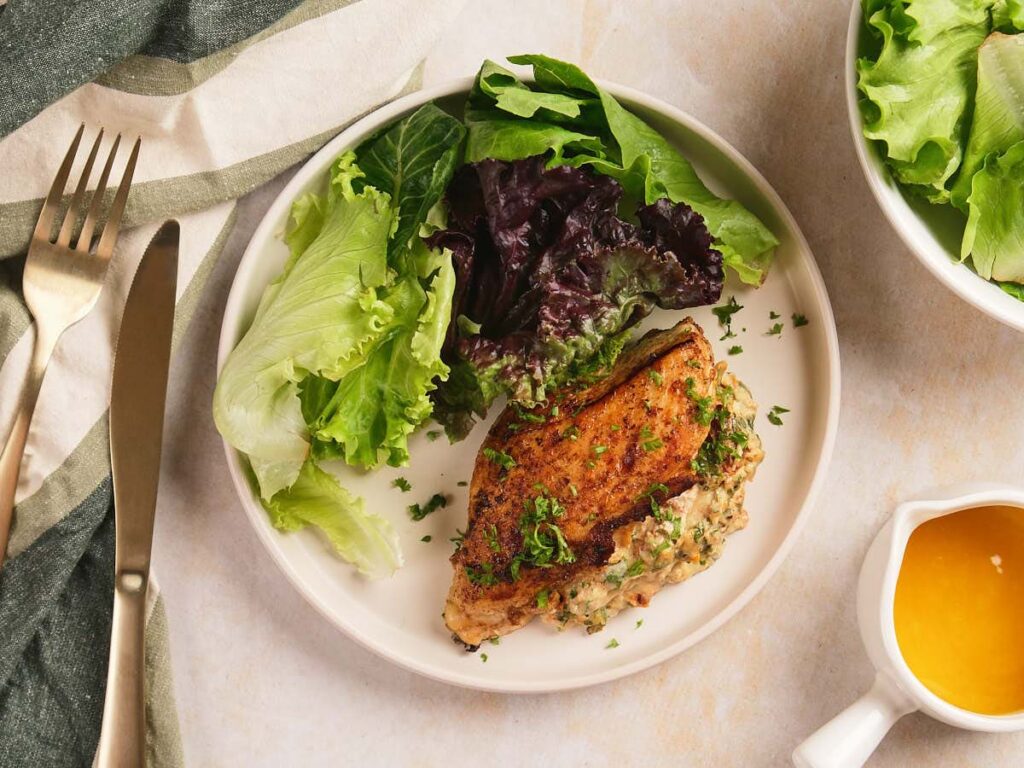 A plate with stuffed chicken breast garnished with herbs and served with mixed leafy greens.