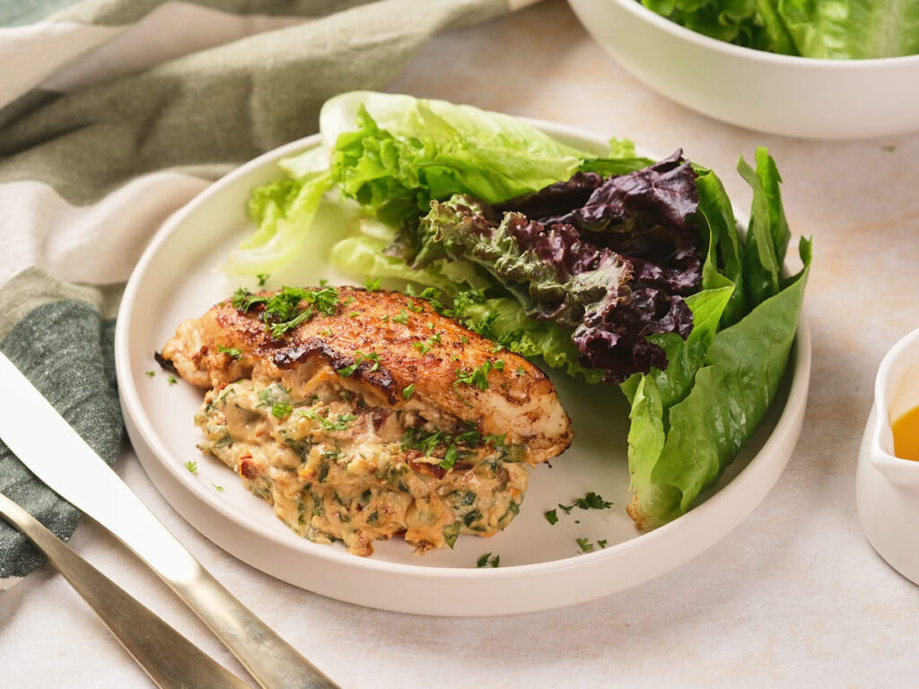 A plate with stuffed chicken breast garnished with herbs and served alongside a mix of fresh leafy greens.