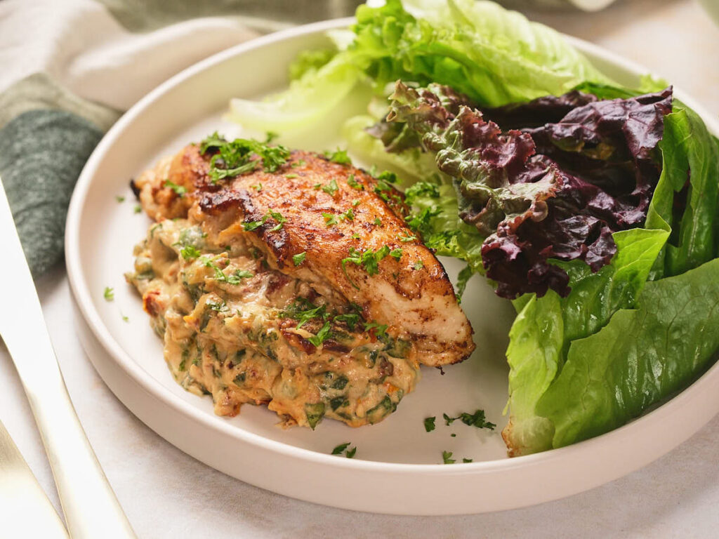 A plate of stuffed chicken breast topped with herbs, served with a side of fresh green and red lettuce leaves.