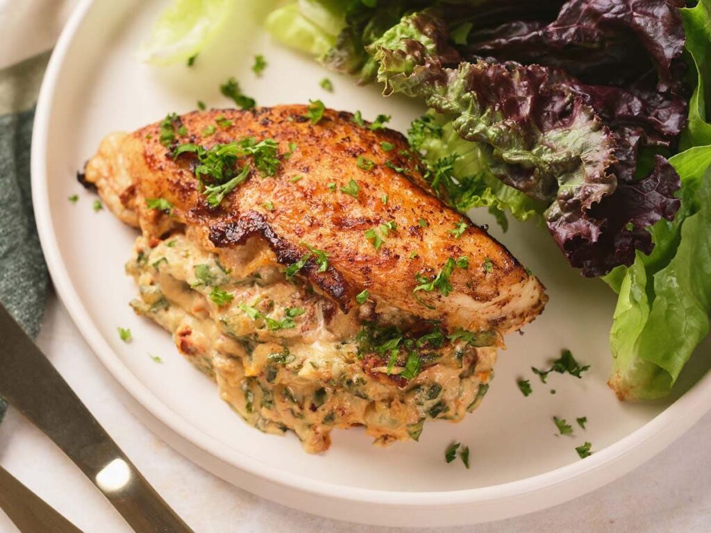 Grilled stuffed chicken breast with creamy spinach filling, garnished with chopped herbs.