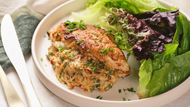 A plate with a cooked stuffed chicken breast garnished with herbs, served alongside fresh green and purple lettuce leaves.