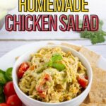 A bowl of homemade chicken salad with cherry tomatoes, cucumber slices, and crackers on a white plate.