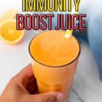 A hand holds a glass of orange juice with a yellow straw, placed on a white surface next to lemon slices; text reads "Quick and Healthy Immunity Boost Juice.
