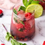 A fruit juice with fresh raspberries, mint and lime and more mint and berries on the background.