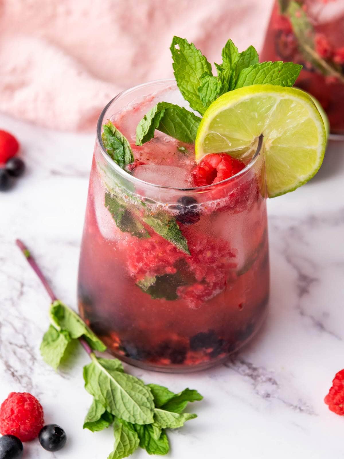 A fruit juice with fresh raspberries, mint and lime and more mint and berries on the background.