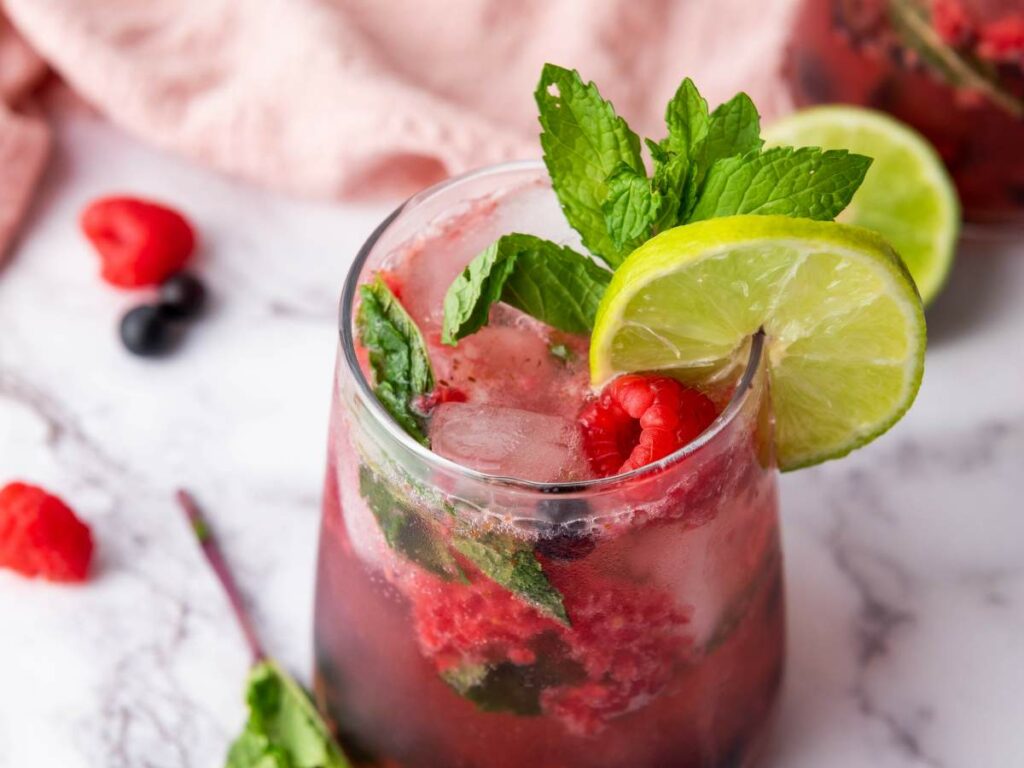 A glass filled with blueberry mocktail with fresh lime and mint on a marble surface.