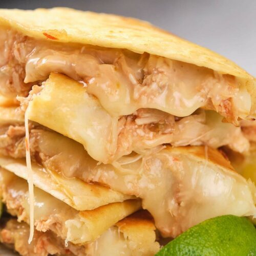 Close-up of stacked chicken quesadillas filled with melted cheese and shredded chicken, with a lime wedge in the foreground.