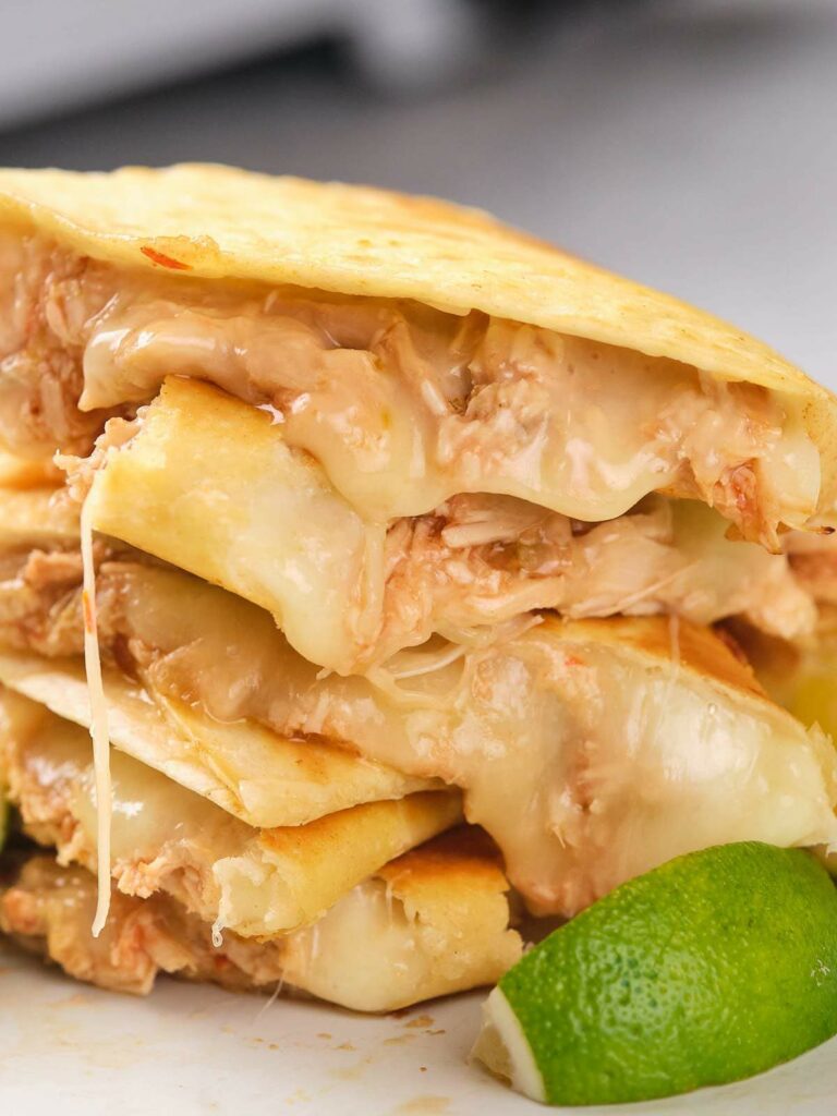 Close-up of stacked chicken quesadillas filled with melted cheese and shredded chicken, with a lime wedge in the foreground.