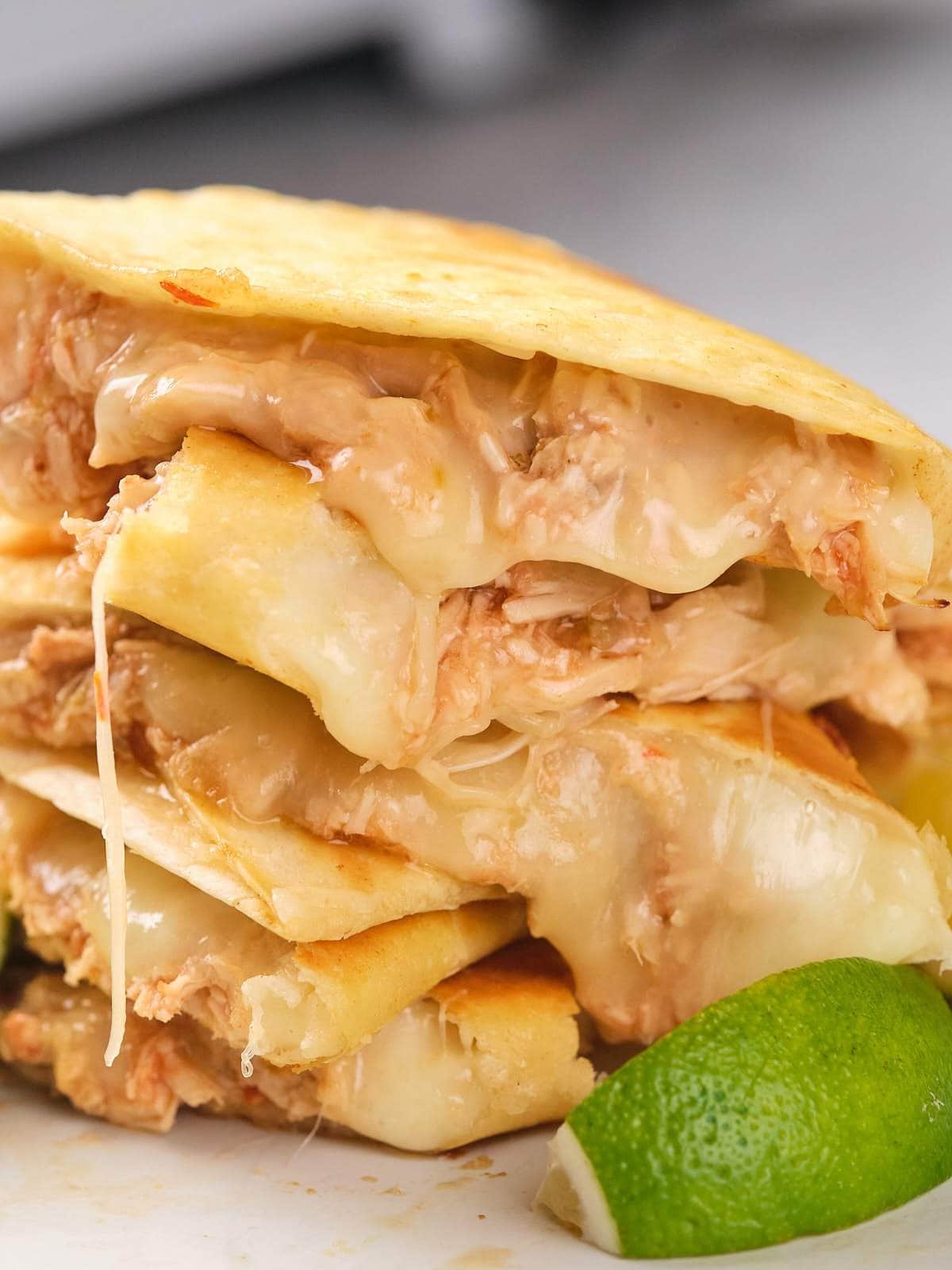 Close-up of stacked chicken quesadillas filled with melted cheese and shredded chicken, with a lime wedge in the foreground.