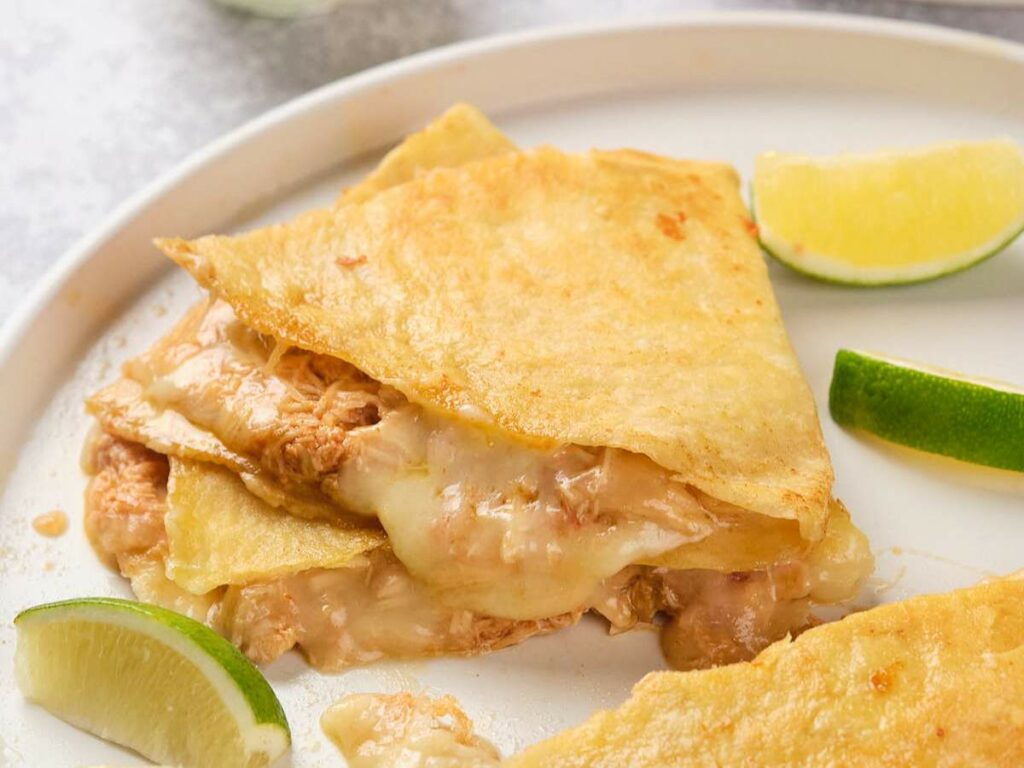 A chicken quesadillas served on a white plate with lime wedges.
