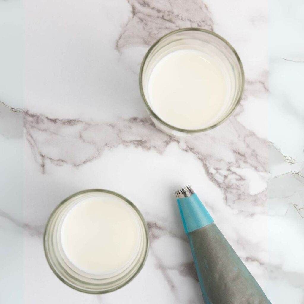 Two glasses of milk and a piping bag on a marble surface.