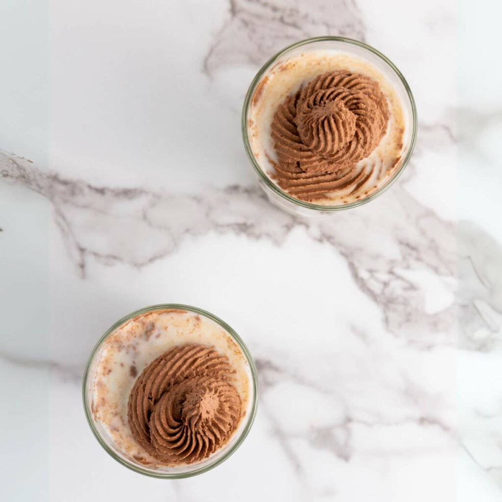 Top-view of two glasses of milk topped with chocolate whipped.