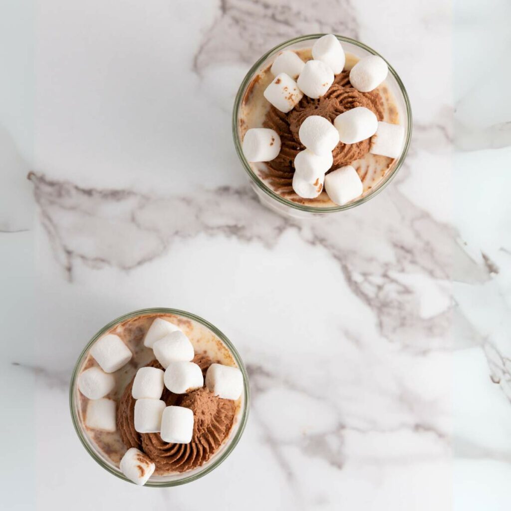 Two glasses of milk topped with chocolate whipped cream and marshmallows.