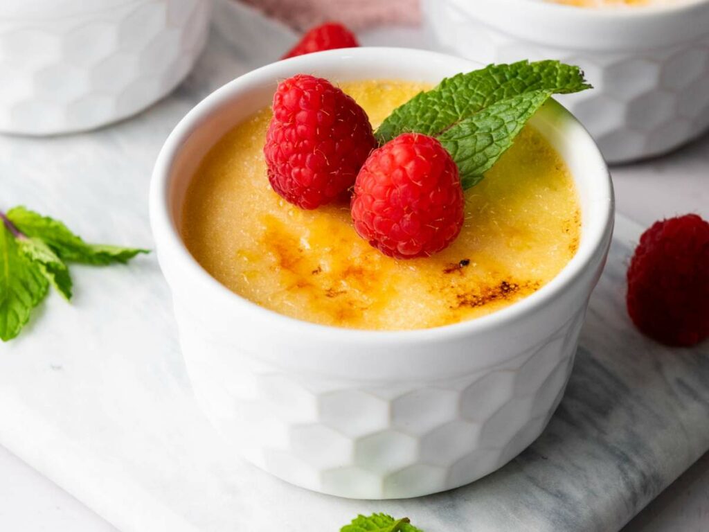 A ramekin of creme brulee topped with two raspberries and a mint leaf.