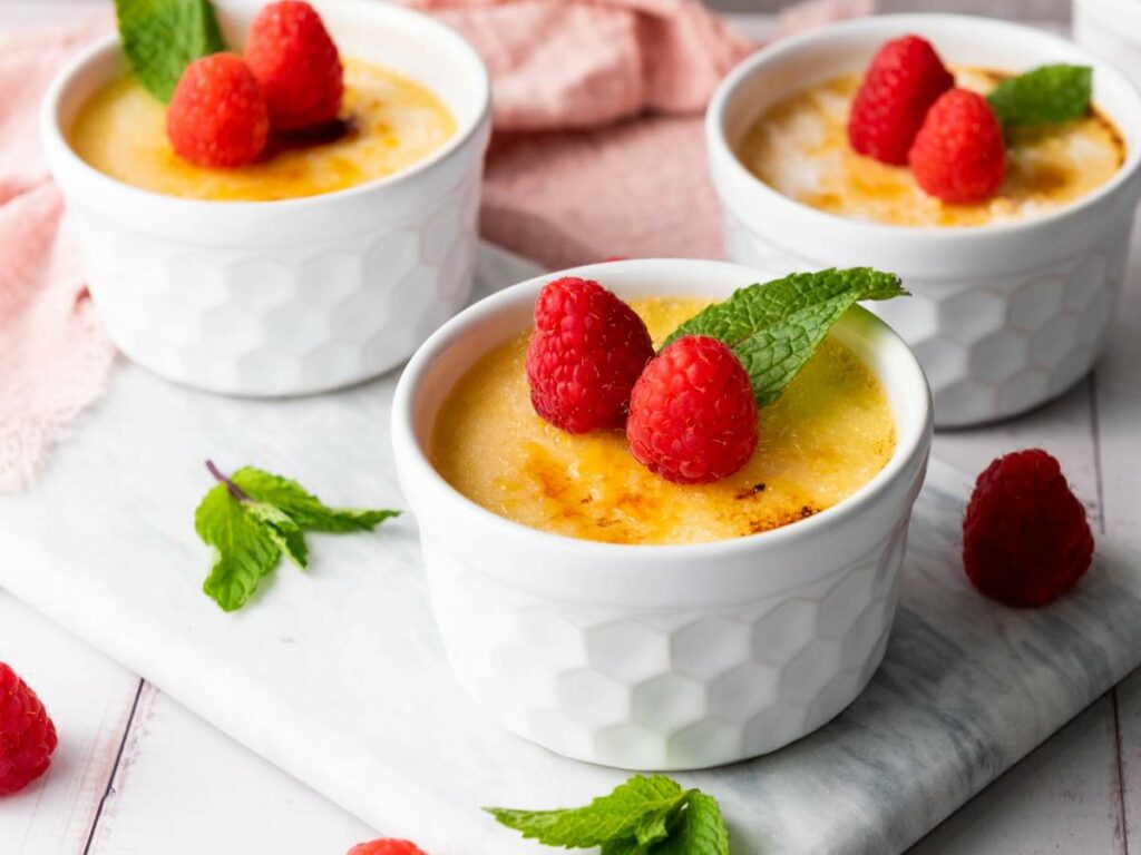 Three ramekins of creme brulee topped with fresh raspberries and mint leave.