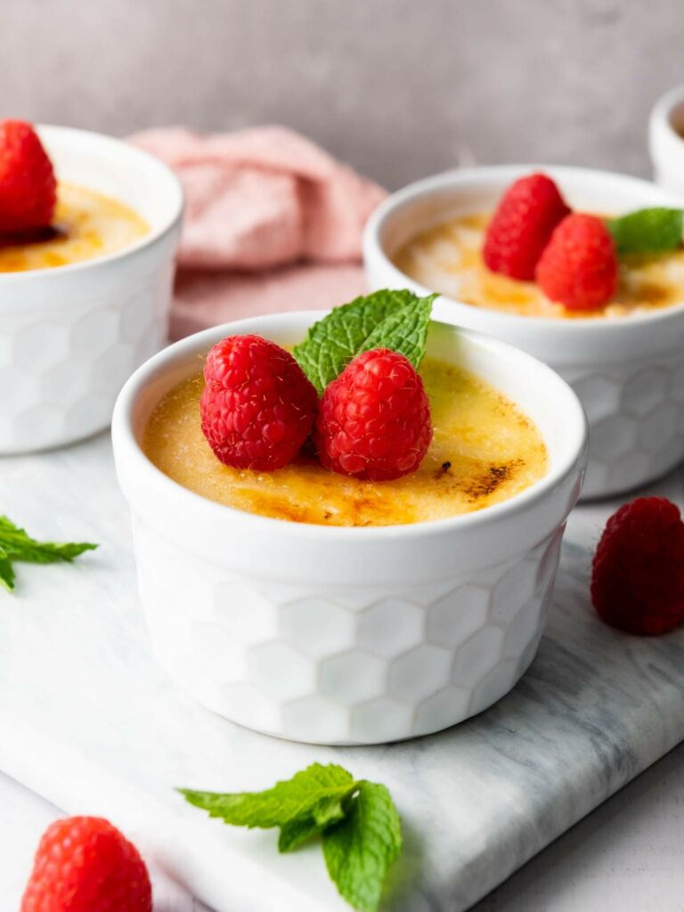 A creme brulee topped with two raspberries and a mint leaf.