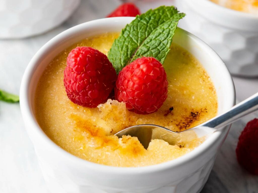 A ramekin of creme brulee topped with two raspberries and a mint leaf.