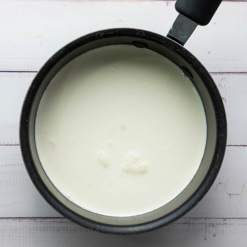 A saucepan filled with milk sits on a white wooden surface.
