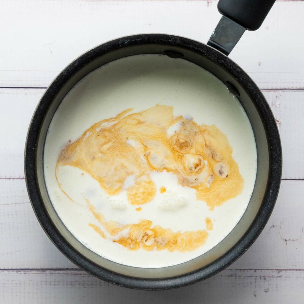 A saucepan containing cream and brown sugar being heated.