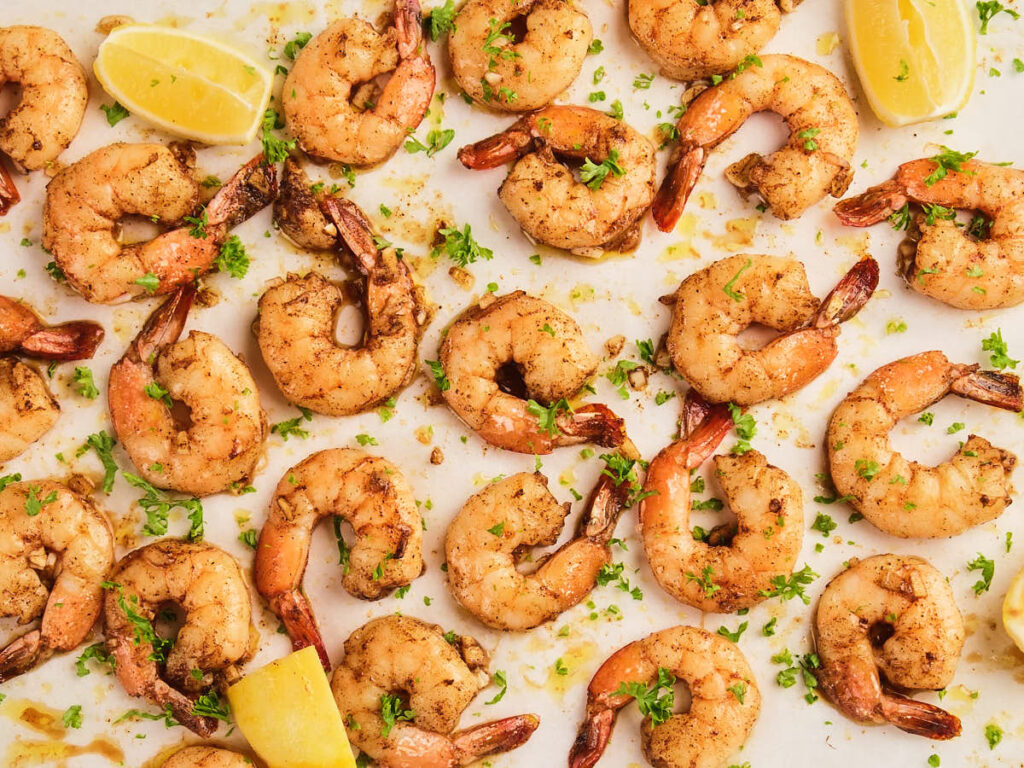 Cooked garlic butter shrimp garnished with chopped parsley are arranged on a white surface.