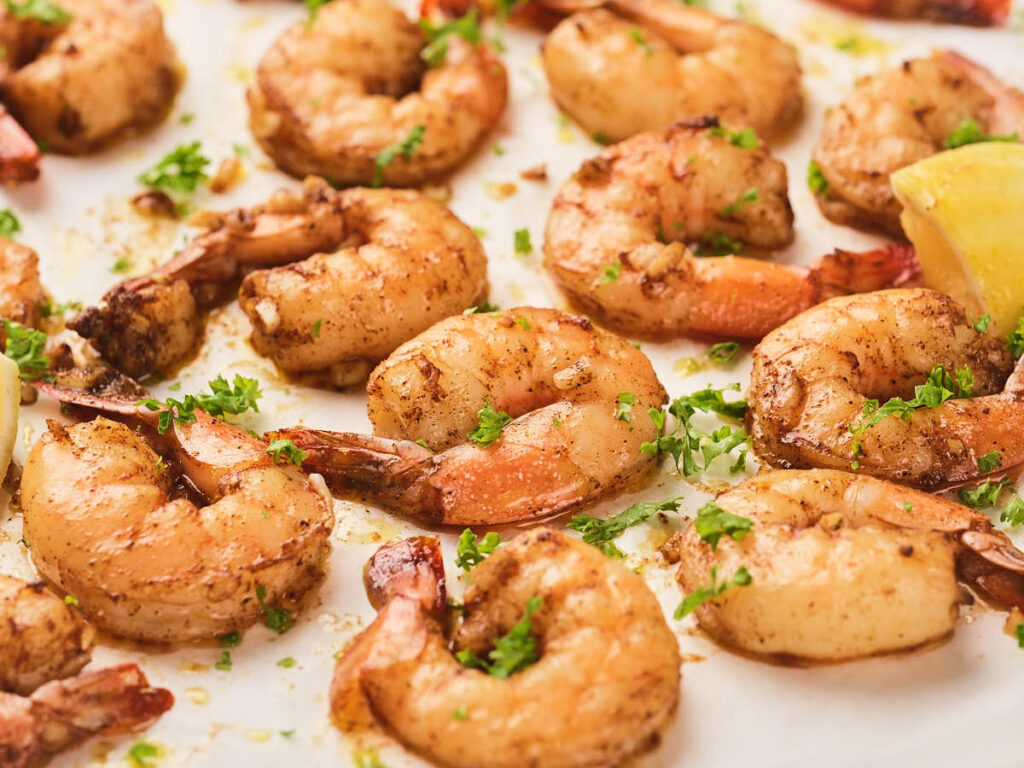 Garlic butter shrimp garnished with chopped parsley with a lemon wedge visible in the corner.