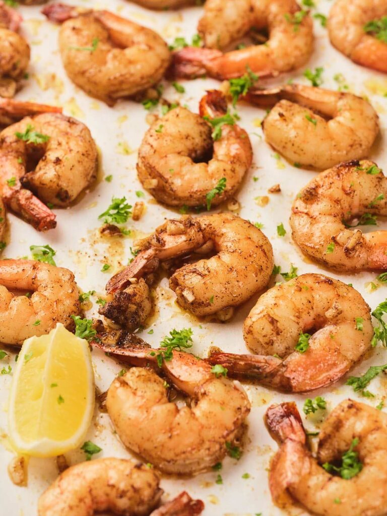 Cooked garlic butter shrimp seasoned with herbs and spices are arranged on a white surface.