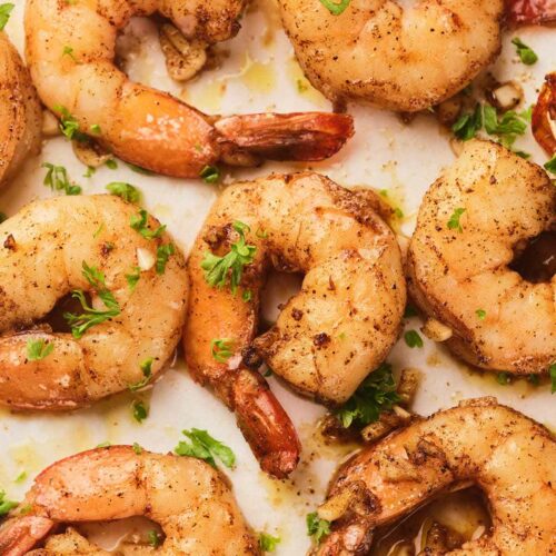 Close-up of cooked of garlic butter shrimp garnished with chopped parsley on a light surface.